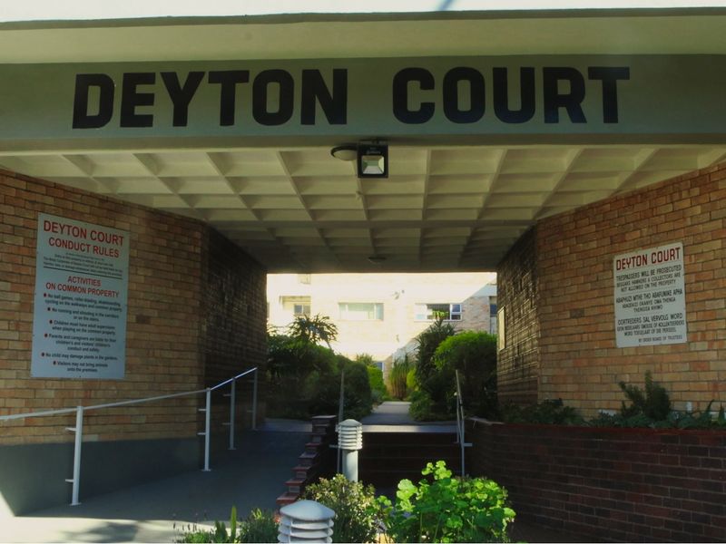 The entrance to Deyton Court apartment complex, featuring a brick facade, covered walkway, and clear signage.
