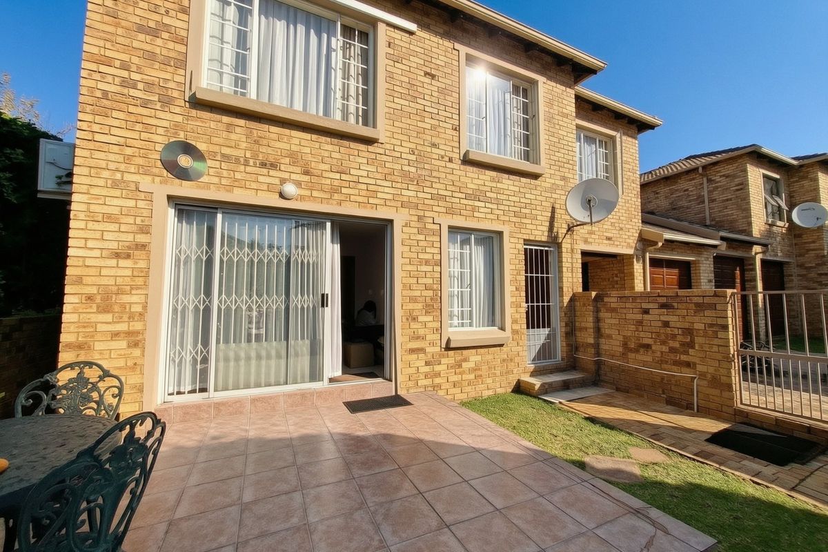 Rear view of a face brick townhouse featuring a tiled patio, sliding door access, and a small private garden area.