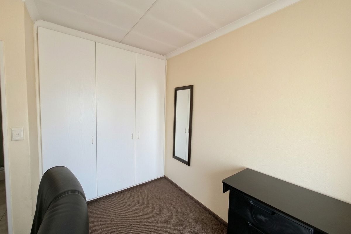 A bedroom featuring neutral walls, carpeted flooring, and white built-in cupboards providing ample storage space.