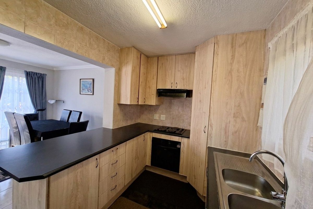 Functional kitchen featuring light wood-look cabinetry, dark laminate countertops, built-in oven, gas hob, and a double bowl stainless steel sink.