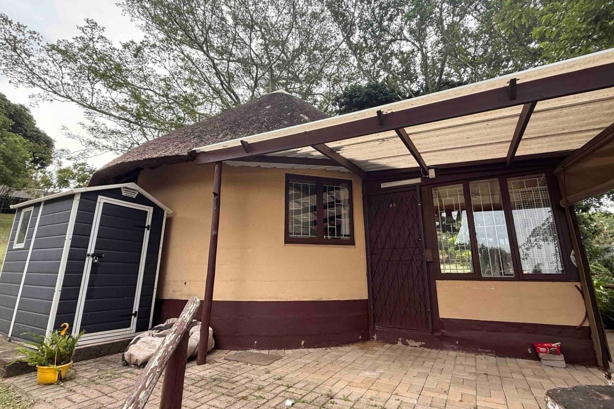 Exterior view of a circular dwelling featuring a thatched roof, paved patio area, and covered walkway with security fixtures.