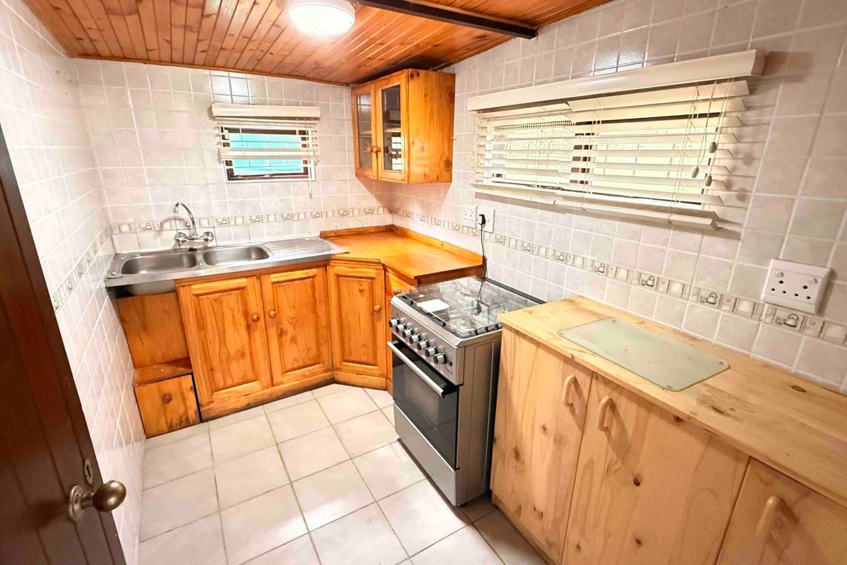 A functional kitchen featuring wooden cabinetry, a double basin sink, a freestanding gas stove, and tiled splashbacks with a classic wooden ceiling finish.
