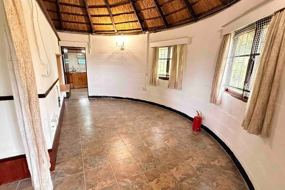 A circular living area featuring a traditional thatched roof, tiled flooring, and security-fitted windows, offering a unique architectural space ready for renovation.