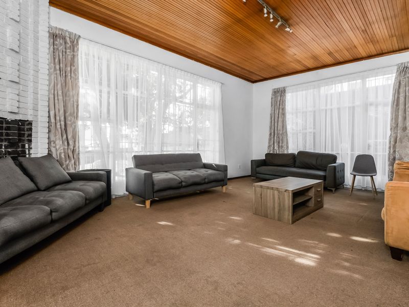 Spacious living room featuring a distinctive timber-clad ceiling, a brick fireplace, and large windows that provide ample natural light.