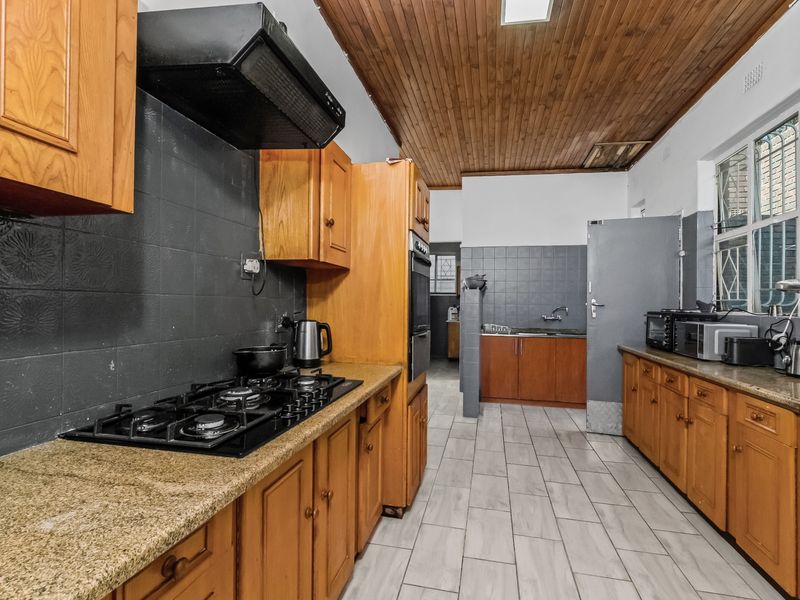 A functional kitchen featuring wooden cabinetry, granite countertops, a gas hob, and a distinctive timber ceiling, offering a classic layout with ample storage.