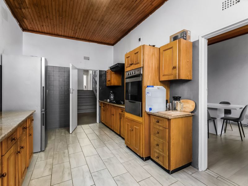 A functional kitchen featuring timber ceilings, built-in wooden cabinetry, granite countertops, and tiled flooring with a direct view into the adjacent living area.
