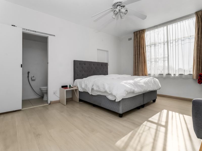 A bright bedroom featuring light laminate flooring, a ceiling fan, and an attached en-suite bathroom with a bidet spray.