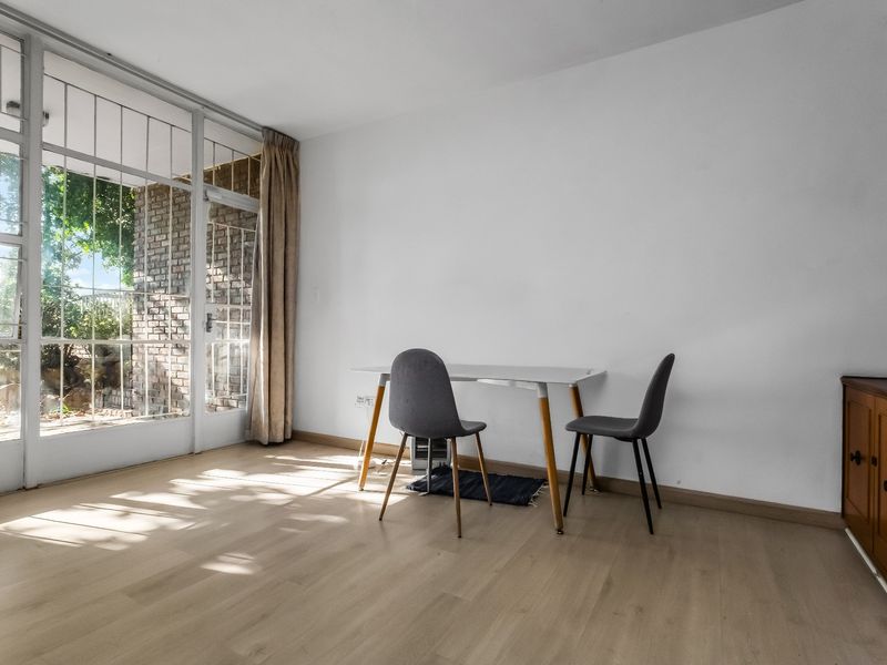 A bright living area featuring light laminate flooring, built-in wooden cabinetry, and a large glass sliding door providing access to the outdoor space.