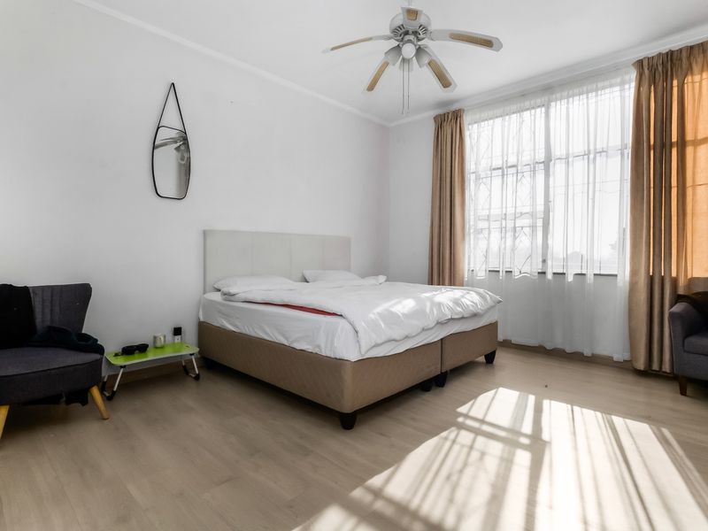 A bright and spacious bedroom featuring light-toned laminate flooring, a ceiling fan, and large windows with security bars.