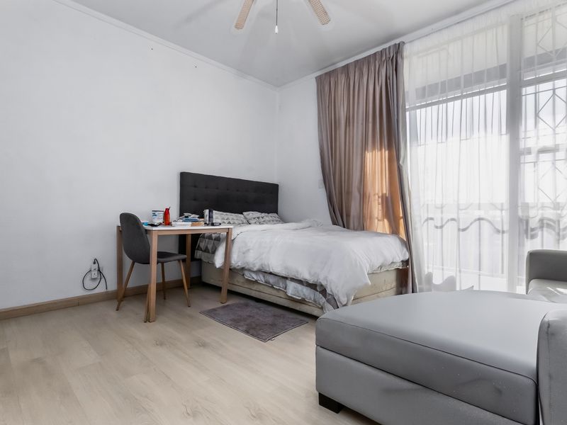 A bedroom featuring light-toned laminate flooring, a ceiling fan, and a large sliding glass door with access to an outdoor area.