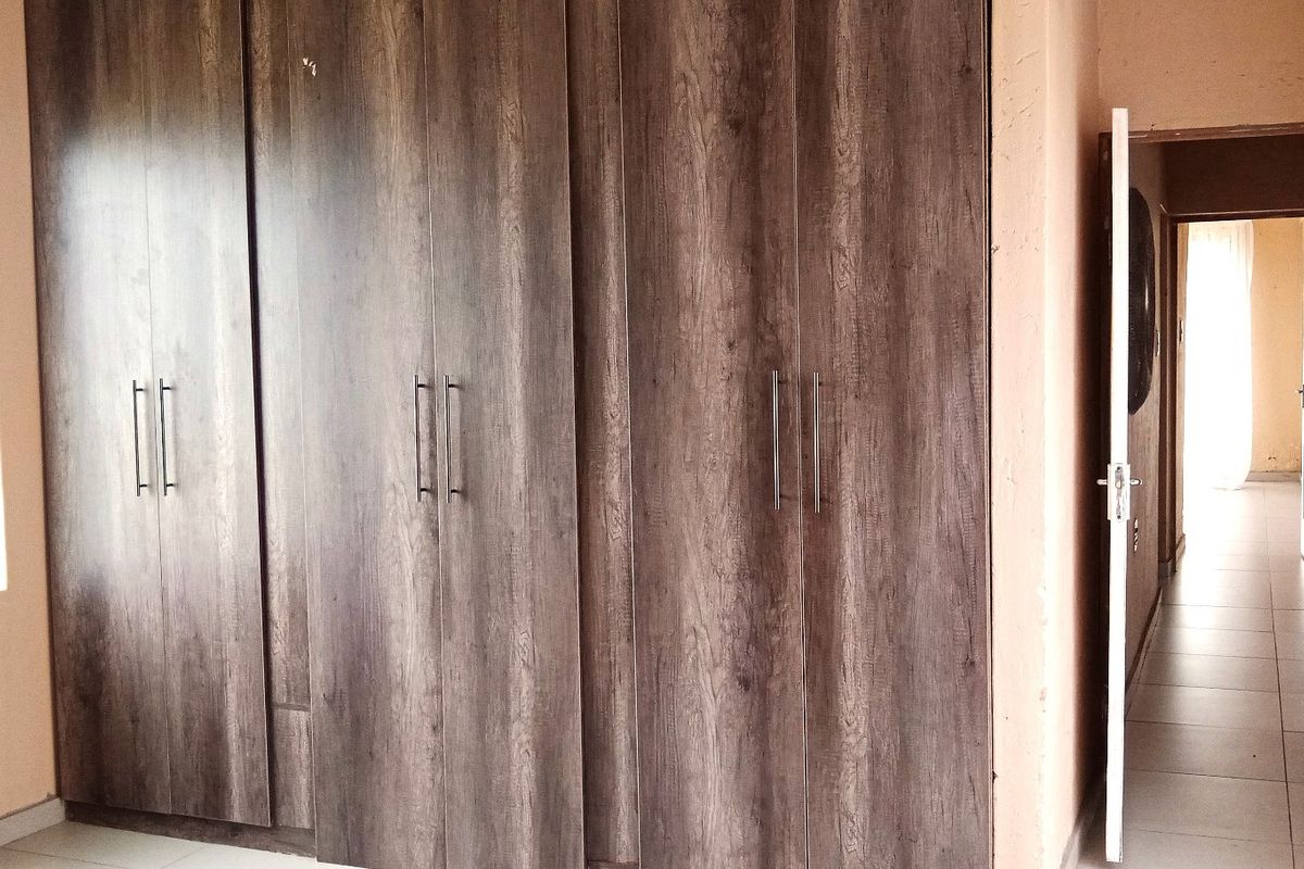 A bedroom featuring dark wood-grain built-in cupboards and tiled flooring, offering a clean and functional space.