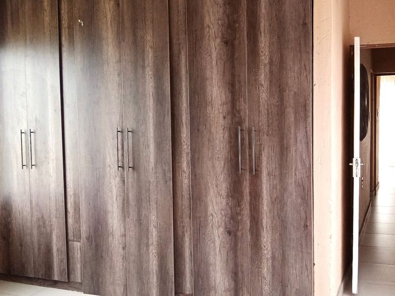A bedroom featuring dark wood-grain built-in cupboards and tiled flooring, offering a clean and functional space.