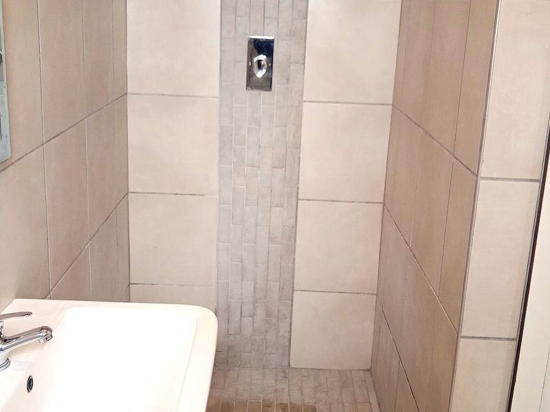 A compact bathroom featuring a wall-mounted basin with chrome mixer tap and a tiled shower enclosure with integrated chrome controls.