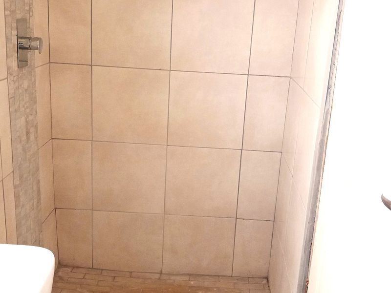 A functional bathroom featuring tiled walls and flooring, a built-in shower mixer, and a basin.