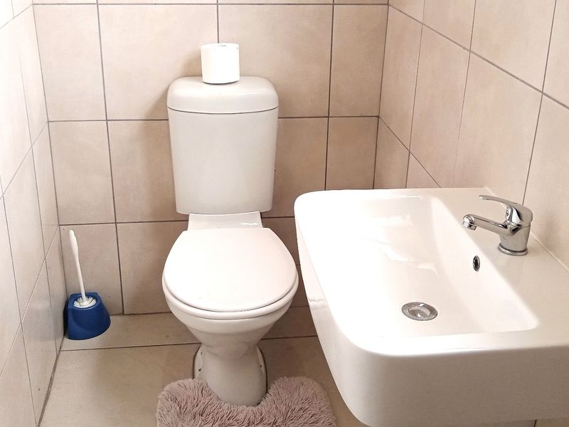 A compact guest bathroom featuring a wall-mounted basin with a chrome mixer tap and a standard close-coupled toilet, finished with neutral ceramic tiling.