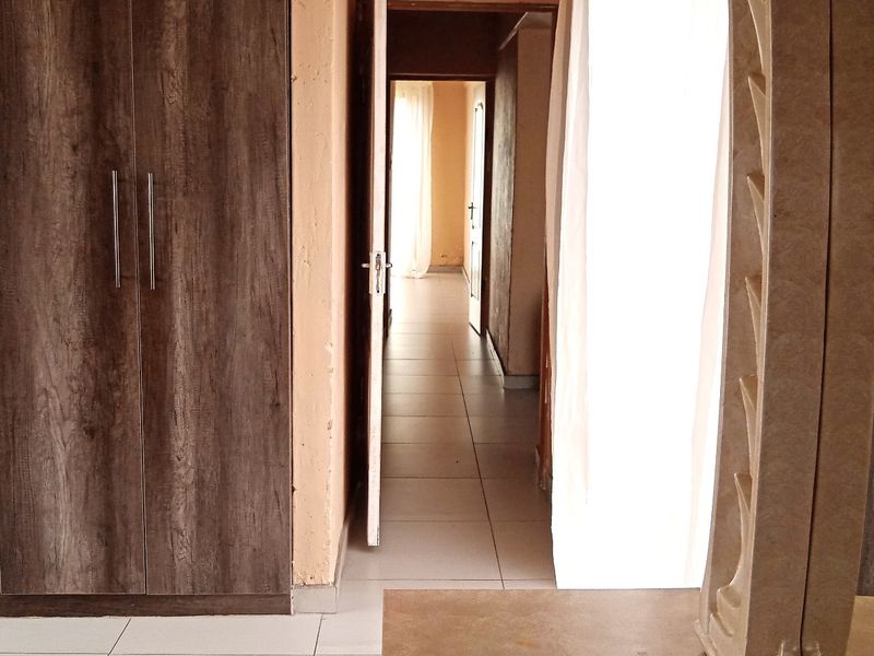 Bedroom featuring built-in wooden cupboards and tiled flooring, with a doorway leading to a connecting hallway.