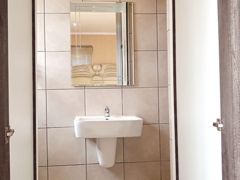 A compact bathroom featuring a white pedestal washbasin and wall-mounted mirror, finished with neutral ceramic wall tiling.