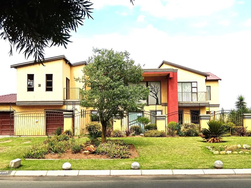 A double-story residential property featuring a paved driveway, double garage, and balcony, set behind a secure wrought iron fence with a landscaped front garden.