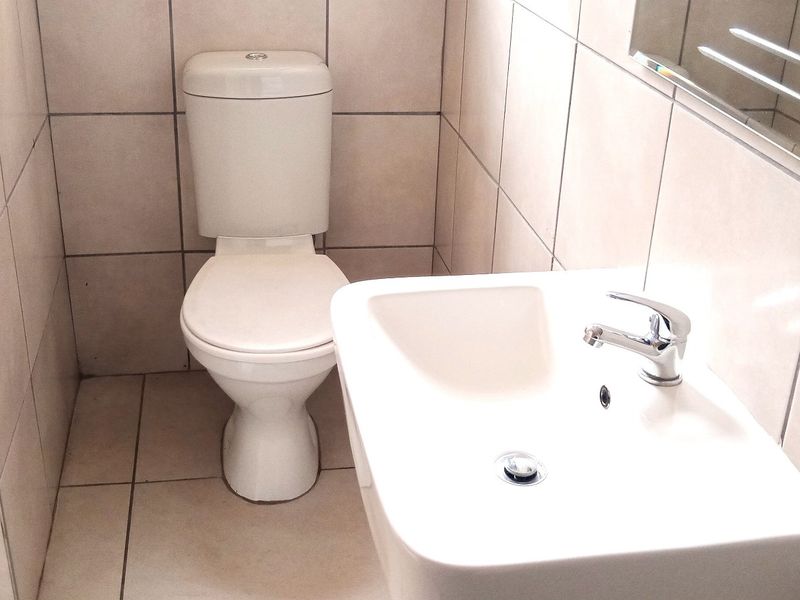 A compact bathroom featuring neutral ceramic wall and floor tiles, a standard white toilet, and a wall-mounted washbasin with a chrome faucet.