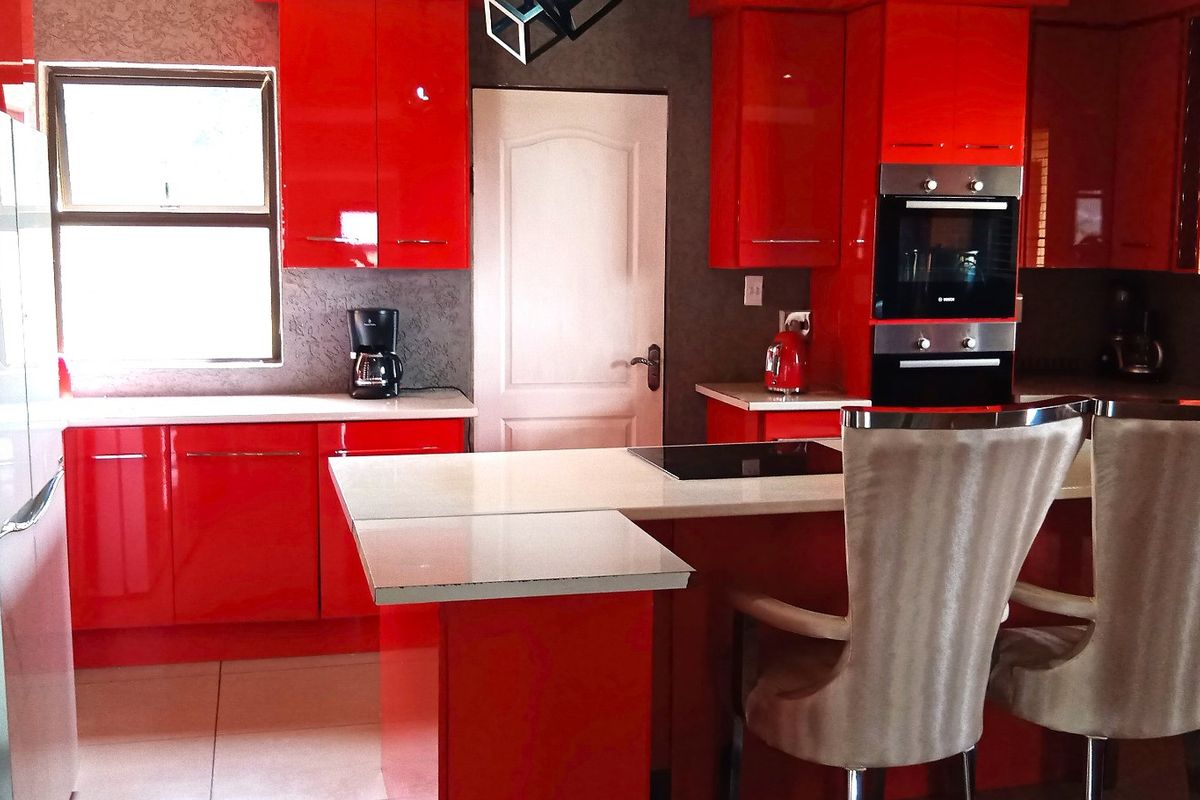 Modern kitchen featuring high-gloss red cabinetry, stone countertops, a central island, and integrated oven, offering a bold and functional culinary space.