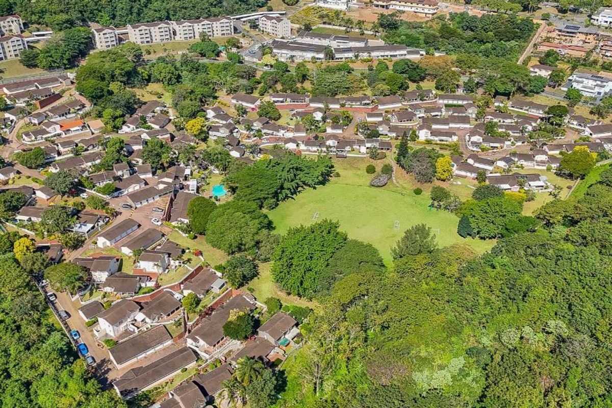 An aerial view of a residential townhouse complex featuring extensive green spaces, mature trees, and organized housing units within a landscaped estate.
