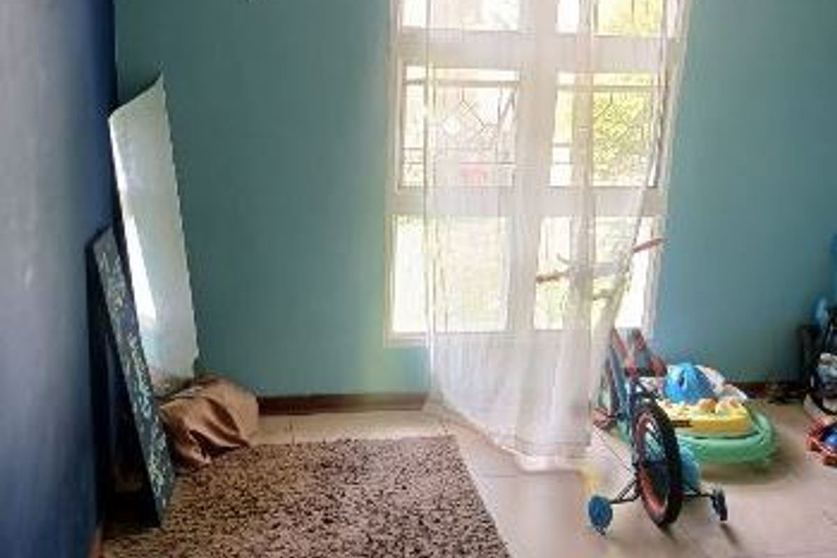 A living area featuring tiled flooring, a ceiling fan, and a window with security bars, currently vacant and awaiting a fresh update.
