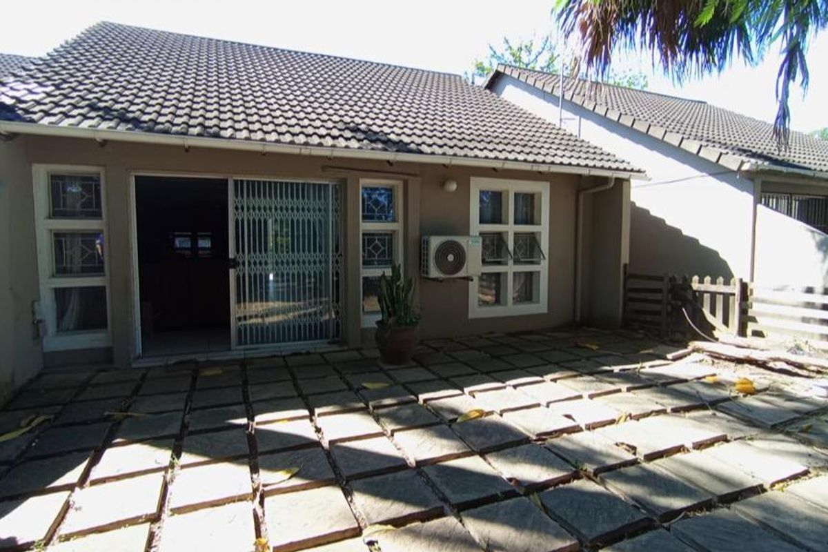 Rear exterior view of the townhouse featuring a paved patio area, security gate, and wall-mounted air conditioning unit.