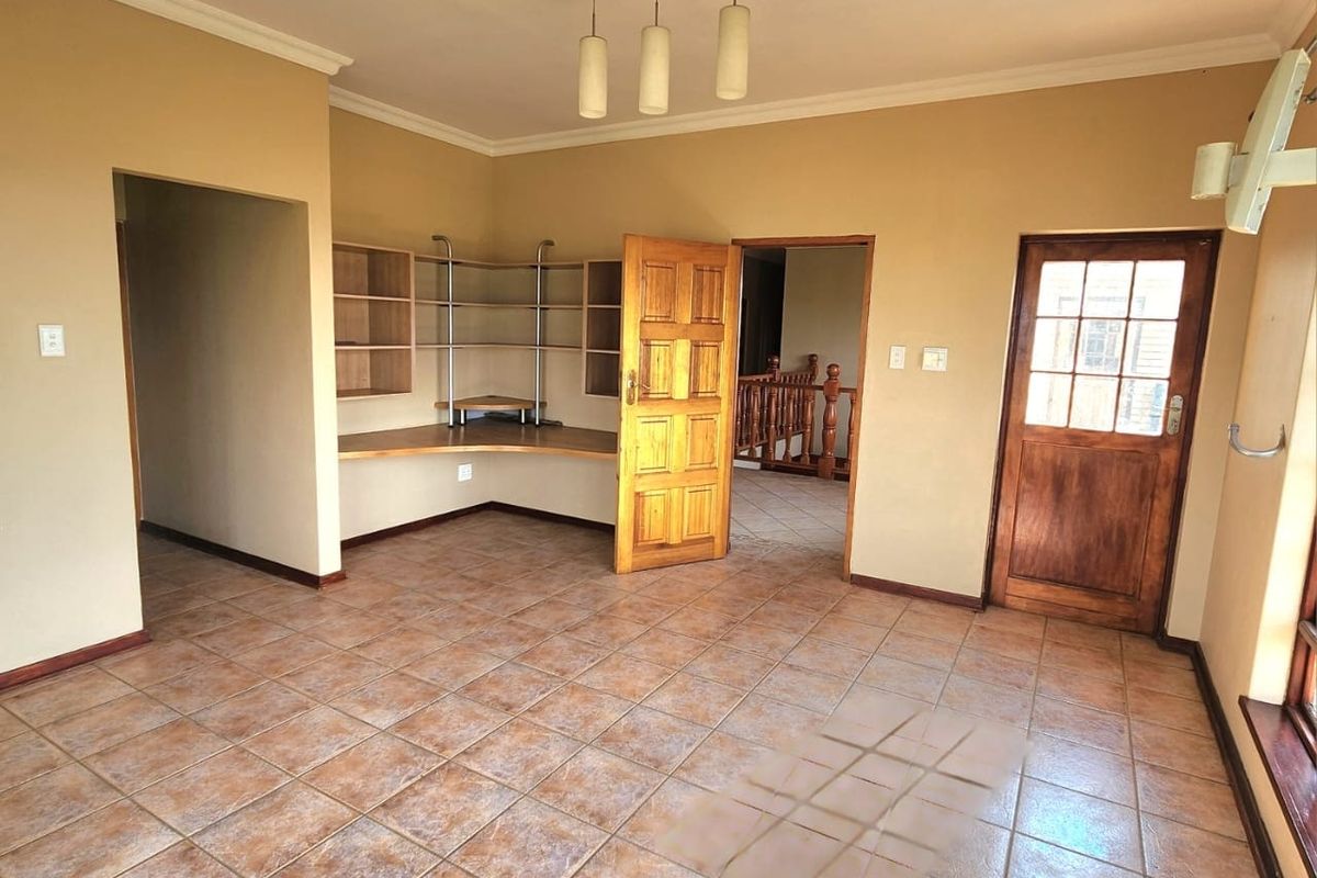 An empty living area featuring tiled flooring, a built-in desk with shelving, and a timber door leading to an adjacent space.