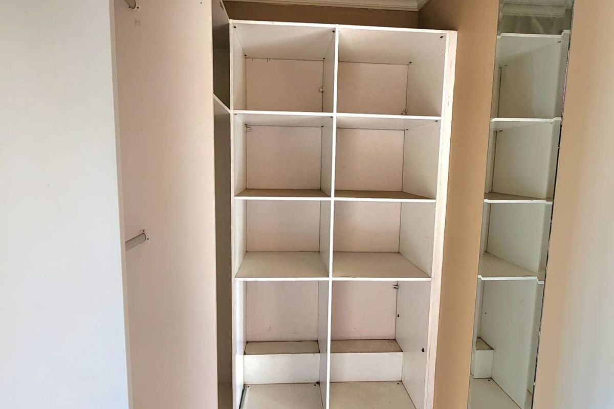 A walk-in closet or bedroom storage area featuring built-in shelving, hanging rails, and a full-length mirror with tiled flooring.