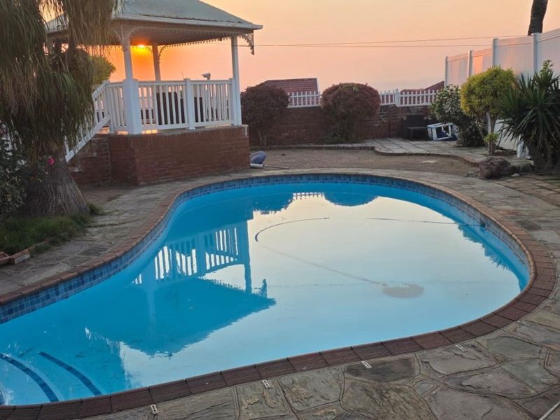 Outdoor pool area featuring a swimming pool, paved surround, and a raised gazebo structure, set within a fenced garden.