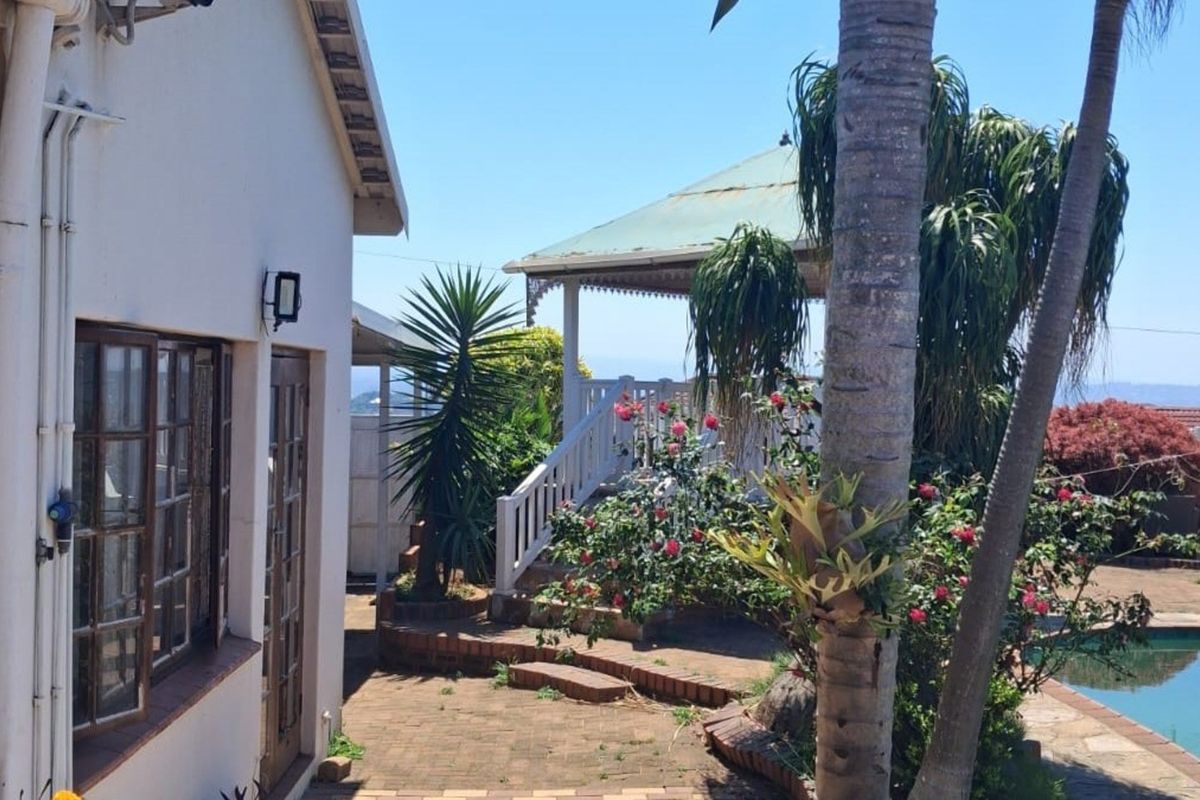 Rear exterior view featuring a swimming pool, brick paved area, and a covered patio structure with timber framed doors and windows.