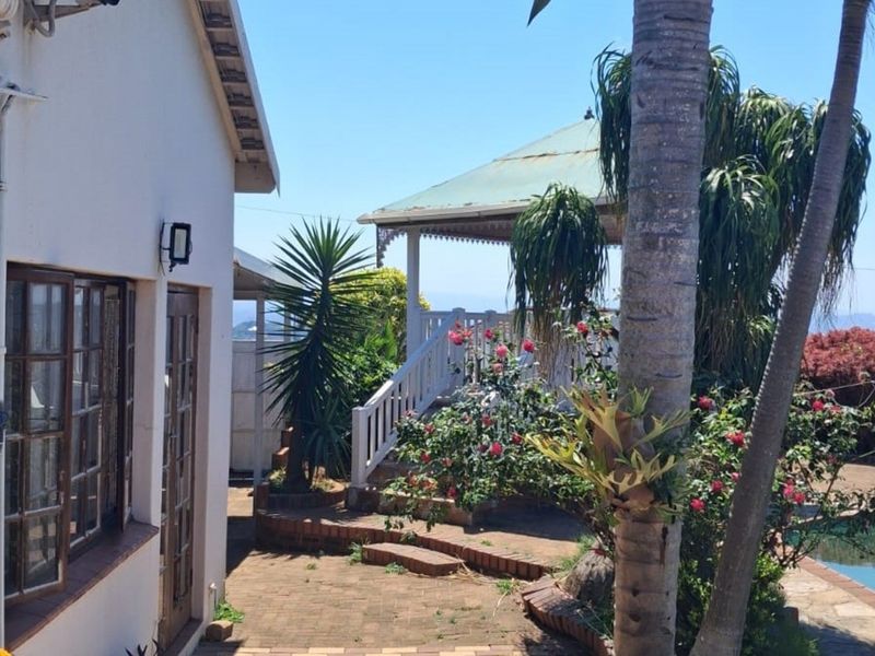 Rear exterior view featuring a swimming pool, brick paved area, and a covered patio structure with timber framed doors and windows.