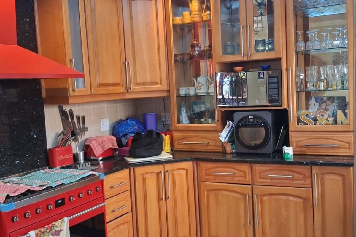 A functional kitchen featuring warm-toned wooden cabinetry, granite countertops, a tiled backsplash, and a distinctive red gas stove with a matching extractor fan.