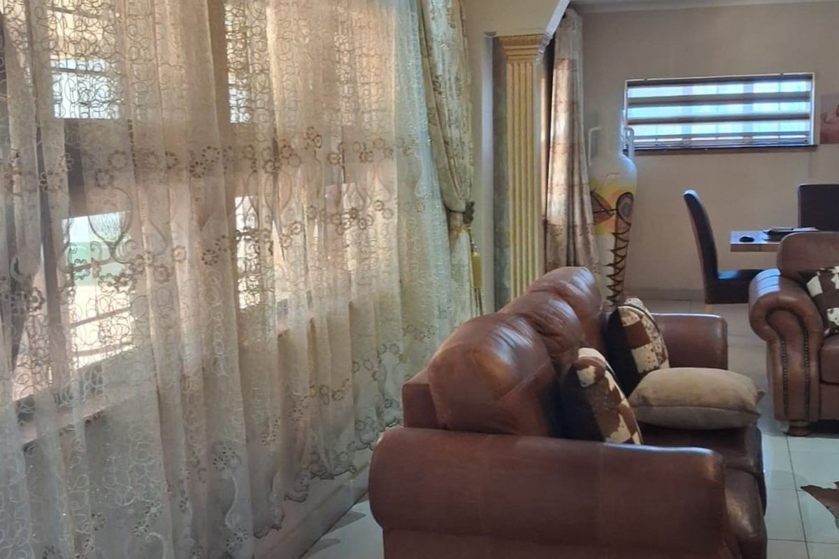 A living room area featuring tiled flooring, a decorative column, and window treatments, providing a functional space for relaxation.