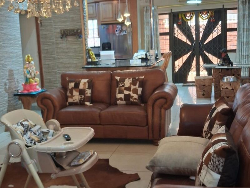 An open-plan living area featuring tiled floors, a chandelier, and a seamless transition to the kitchen and entrance with a decorative security gate.