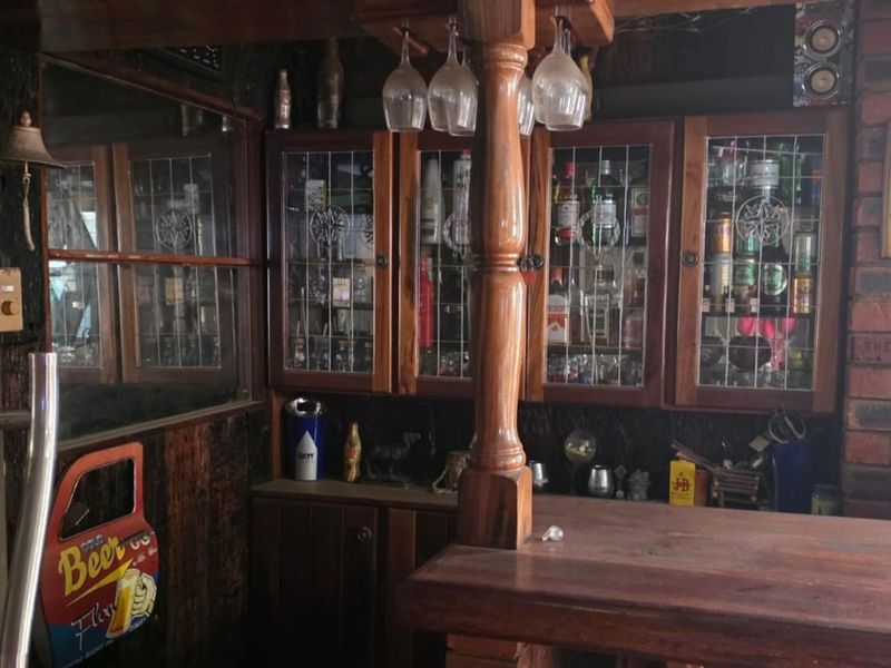 A dedicated home bar area featuring a built-in timber counter, glass-fronted display cabinets, and rustic exposed brick wall detailing.