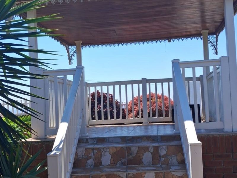 A raised outdoor patio area featuring a timber roof, decorative fretwork, tiled steps, and a white balustrade.