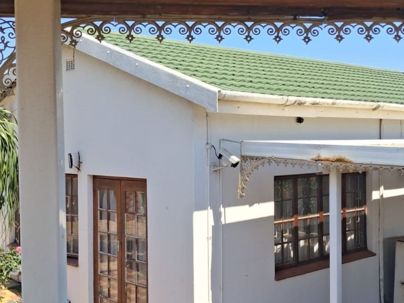 Rear exterior view of the house featuring a green tiled roof, timber framed windows, and decorative wrought iron fretwork on the patio.
