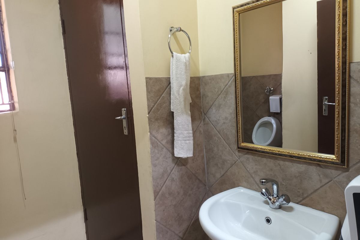 A functional bathroom featuring a pedestal basin with chrome mixer tap, tiled splashback, wall mirror, and a wall-mounted urinal.
