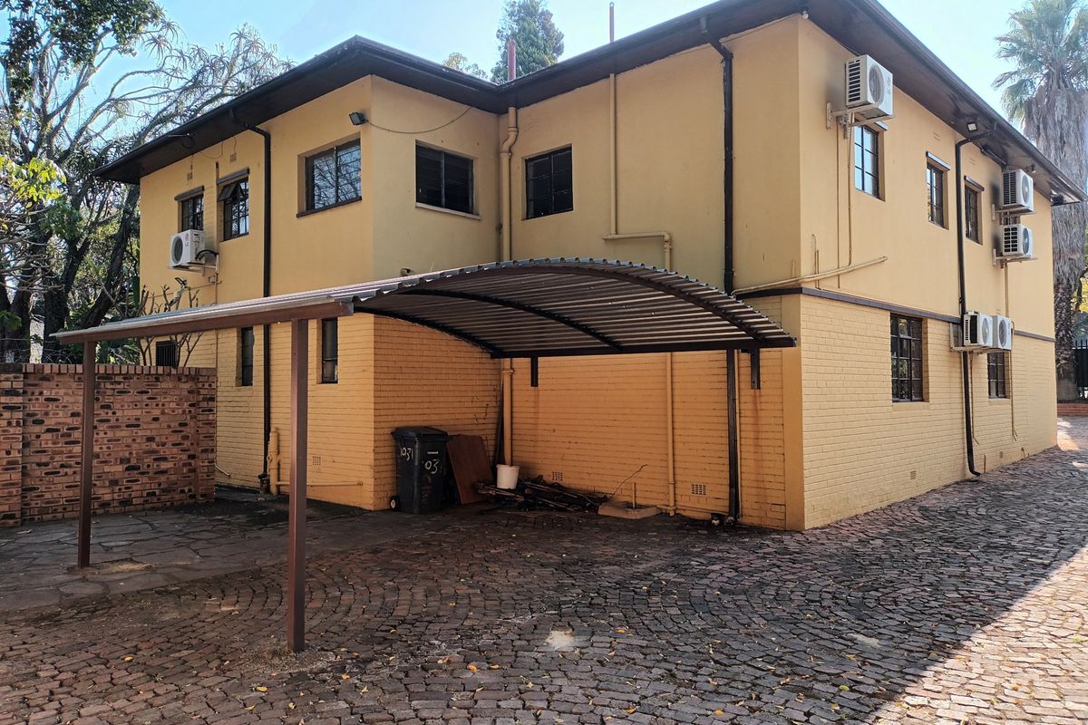 Rear exterior view of the property featuring a curved metal carport, brick paved driveway, and multiple wall-mounted air conditioning units.