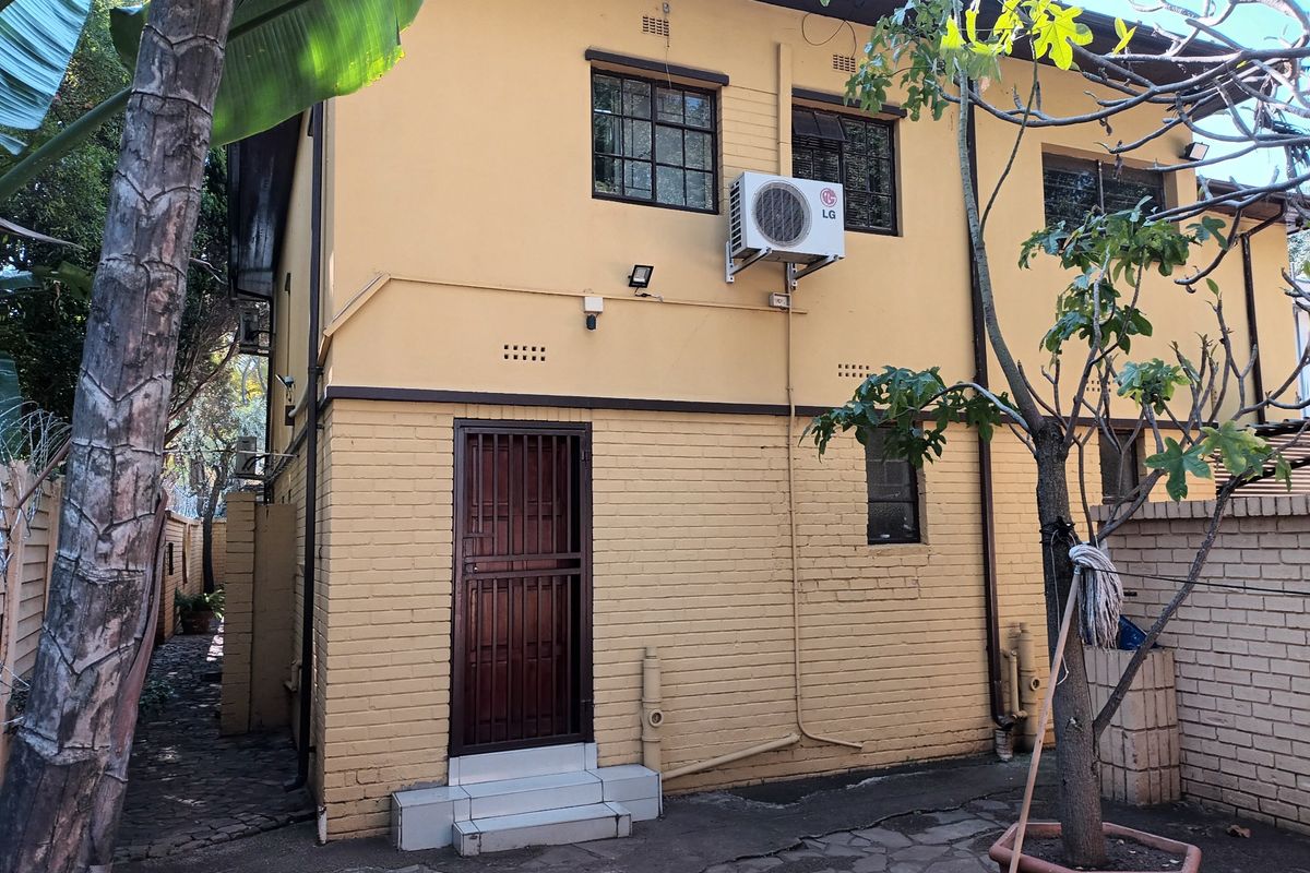 Rear exterior view of the property featuring a brick facade, security gate, and wall-mounted air conditioning unit with a paved courtyard area.