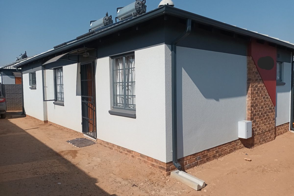 Rear exterior view of the house featuring a solar water heating system, security gates, and a combination of plastered and face-brick finishes.
