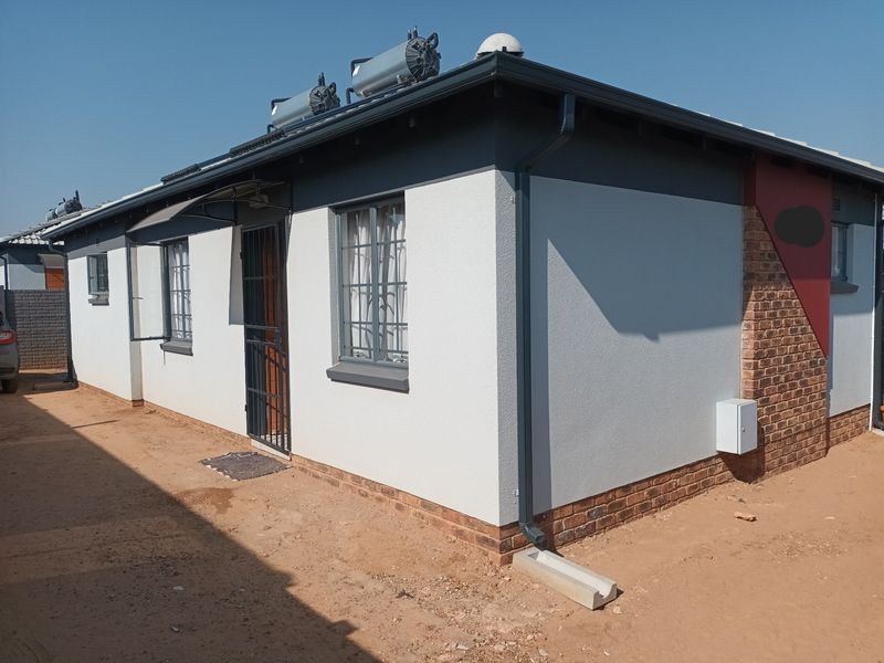 Rear exterior view of the house featuring a solar water heating system, security gates, and a combination of plastered and face-brick finishes.