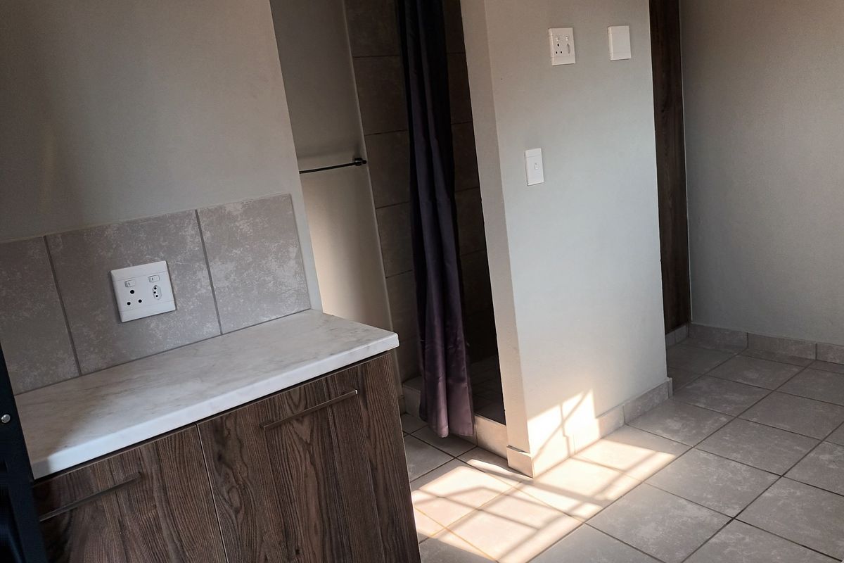 A clean, modern bathroom featuring a built-in vanity with stone-look countertop, tiled splashback, and a separate shower area with neutral ceramic floor tiles.