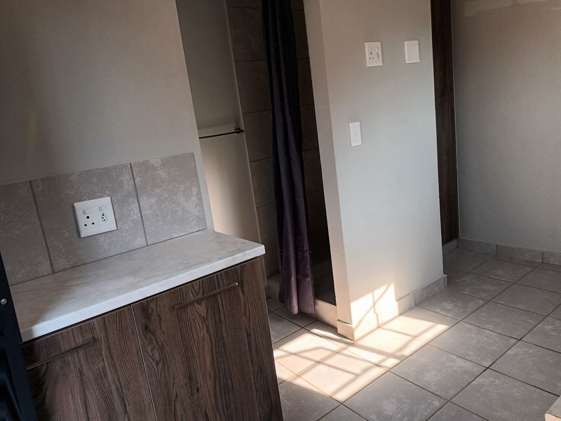 A clean, modern bathroom featuring a built-in vanity with stone-look countertop, tiled splashback, and a separate shower area with neutral ceramic floor tiles.
