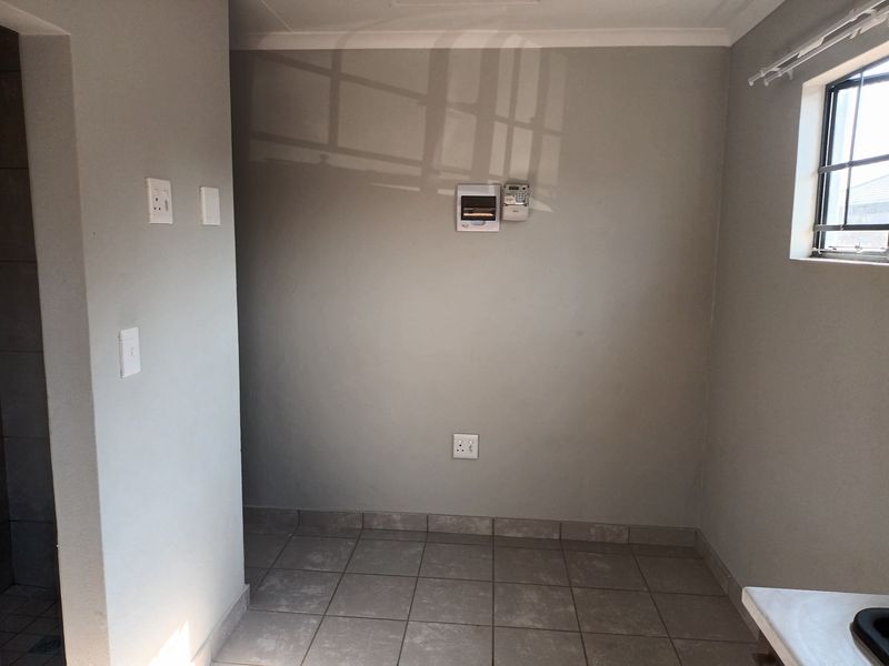 A clean, empty laundry area featuring tiled flooring, a wall-mounted electrical distribution board, and a window with security bars.
