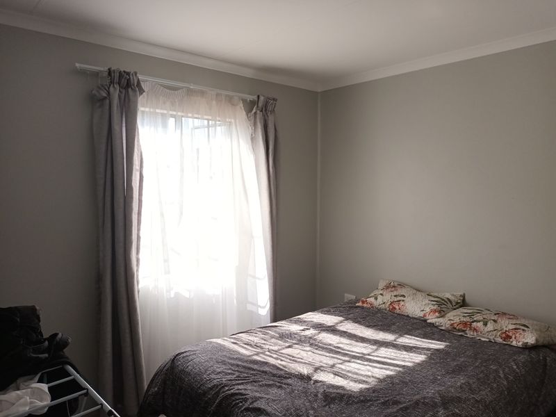 A simple bedroom featuring neutral wall paint, coving, and a window fitted with security bars.