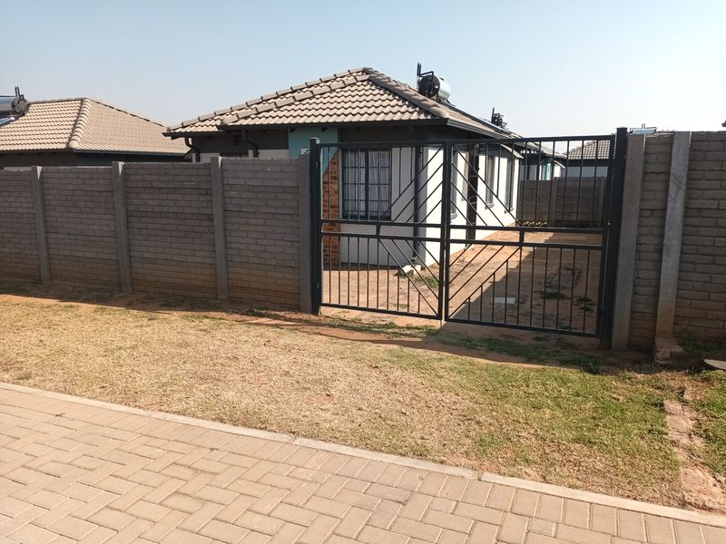 Front view of a residential house featuring a concrete block perimeter wall, metal security gate, and a solar water heater installed on the tiled roof.