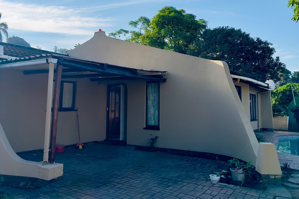 Rear exterior view featuring a covered patio area, paved flooring, and access to an adjacent swimming pool.