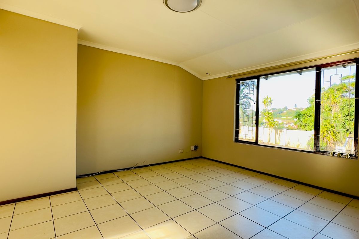 A bright, empty bedroom featuring neutral tiled flooring, large windows with security bars, and a simple flush mount ceiling light.